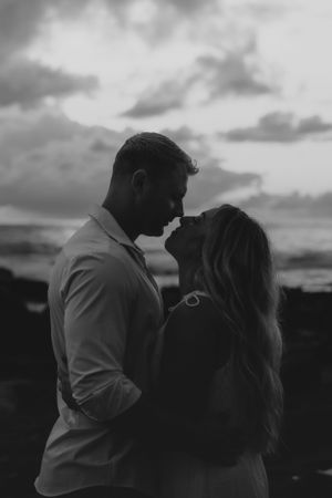 Black and white photo of couple sharing intimate moment during sunset beach photoshoot.
