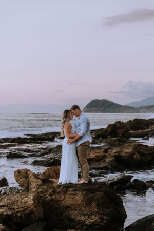Couple shares romantic moment on rocky beach during sunset.