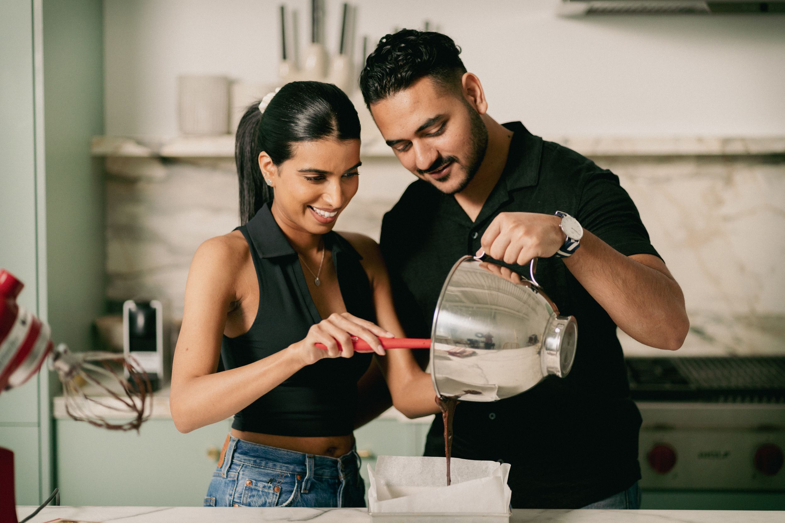 A couple pours ingredients while baking together in a bright modern kitchen.
