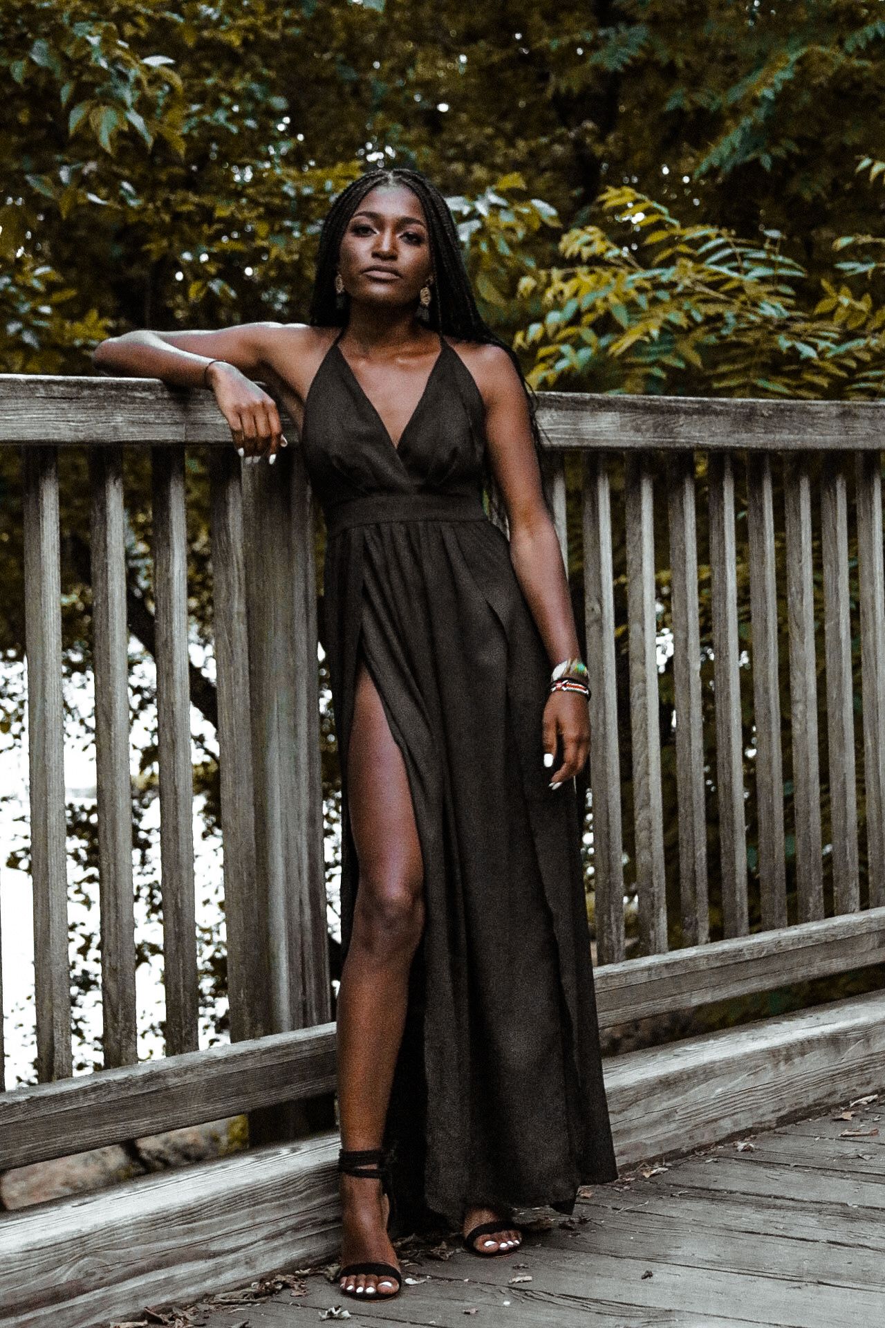 Fashion shoot on wooden deck showcasing elegant black evening dress against natural backdrop.