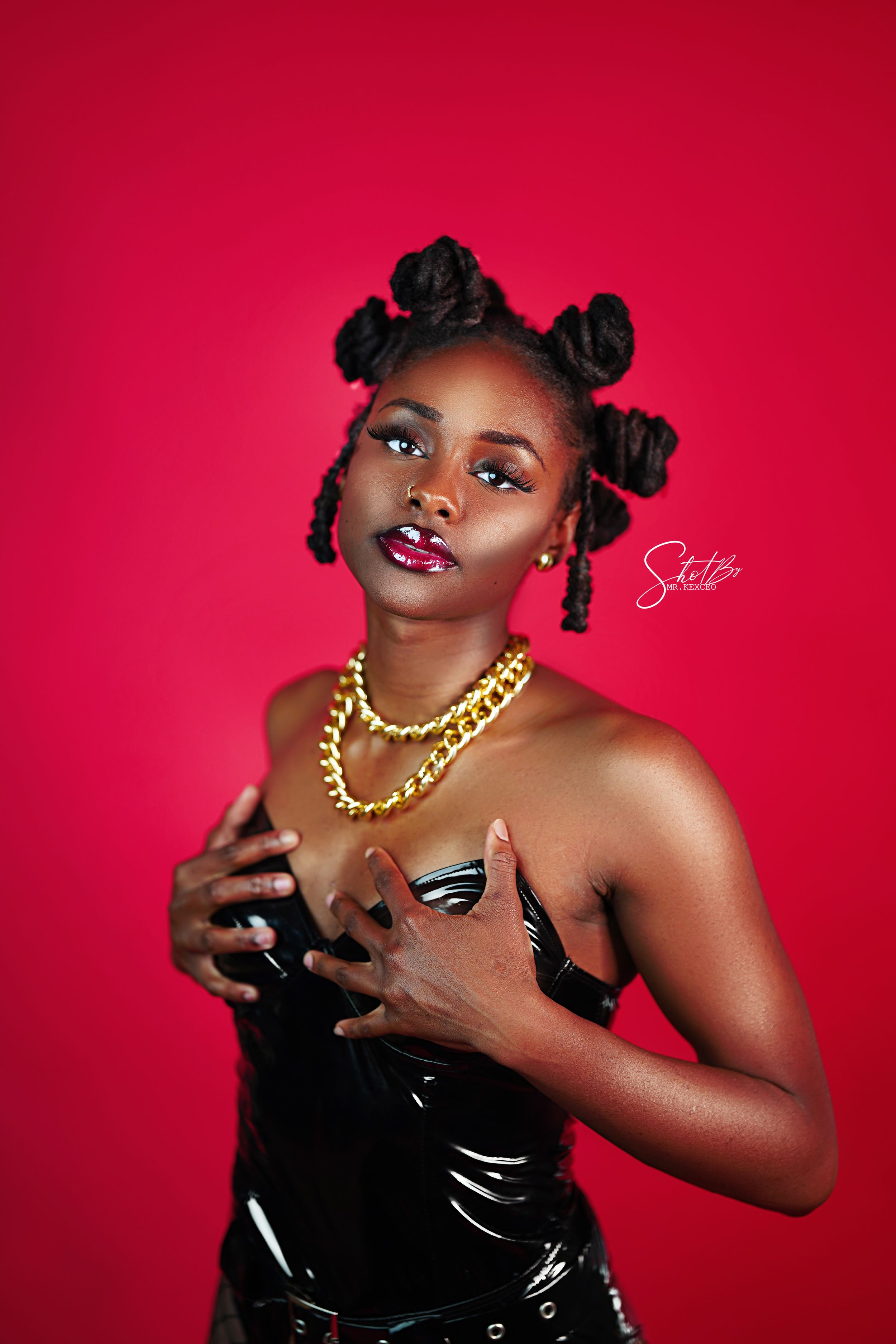 Fashion portrait in black latex dress with gold chain necklace against red background.