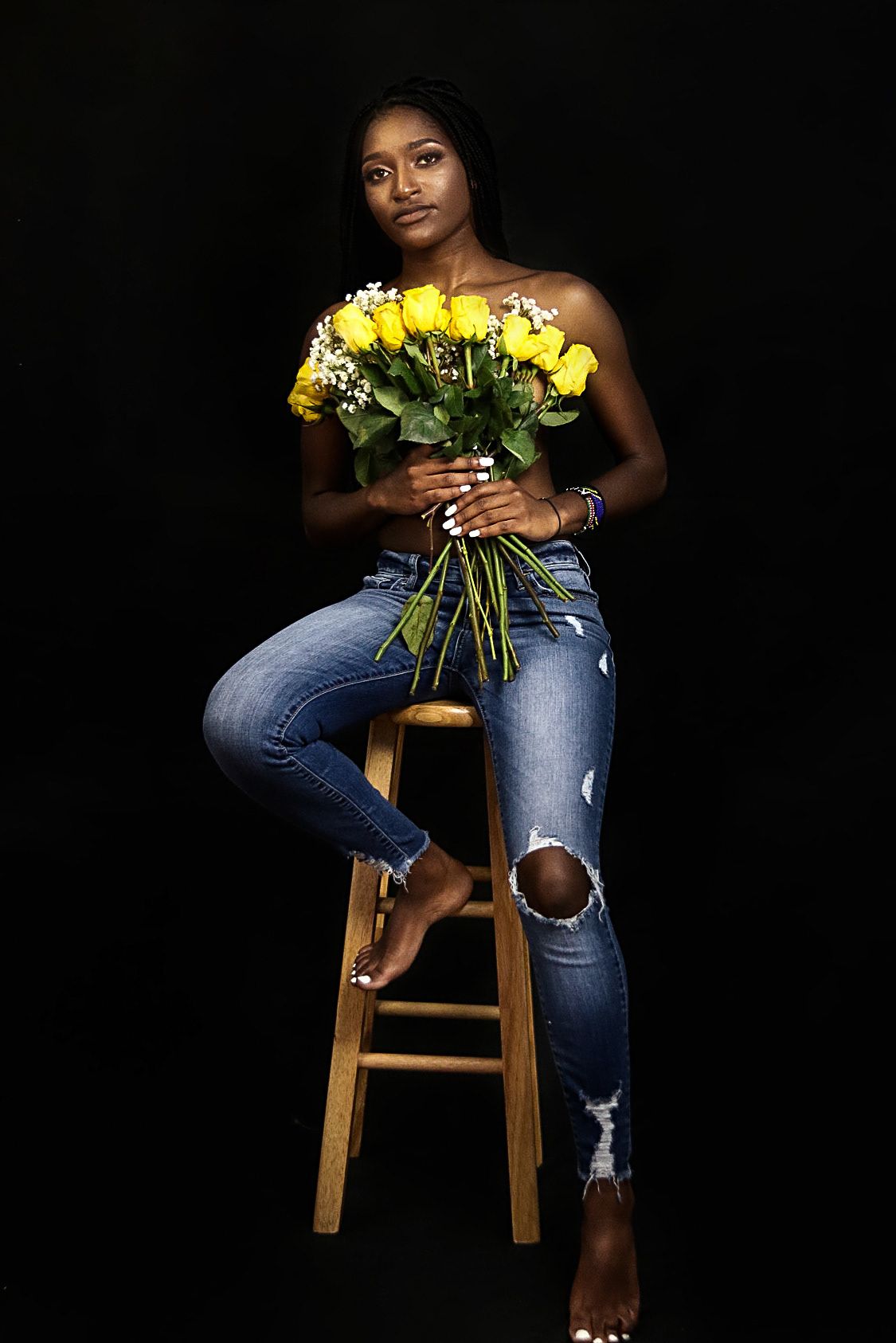 Portrait series showing person holding yellow roses while sitting on wooden stool.
