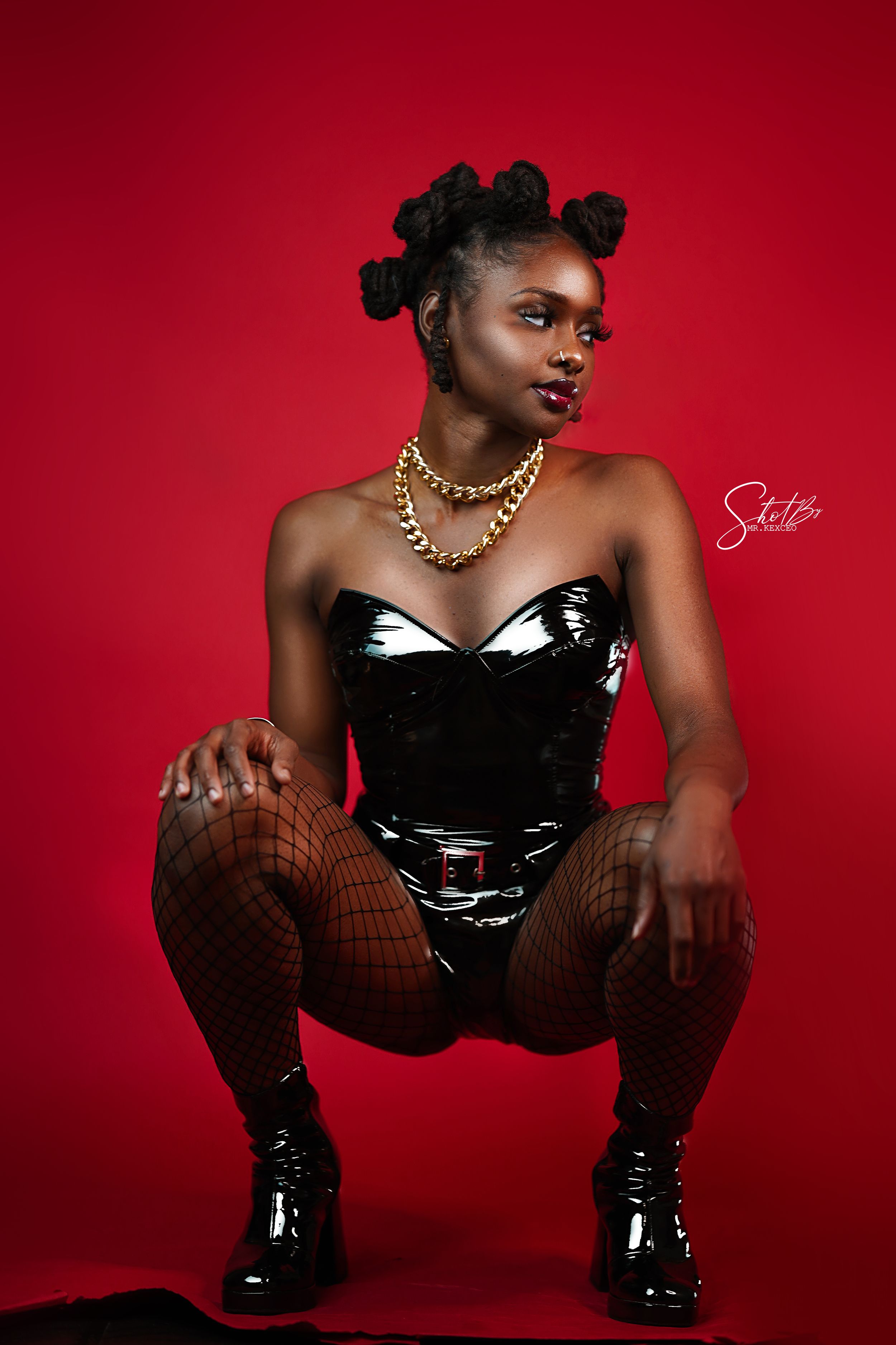 Edgy fashion poses in black latex dress and boots against vibrant red backdrop.