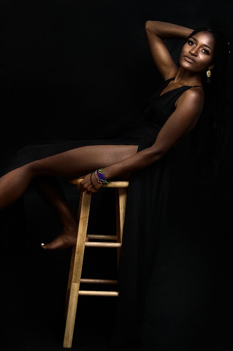 Artistic portrait of a model posing gracefully on a wooden stool against a dark background.