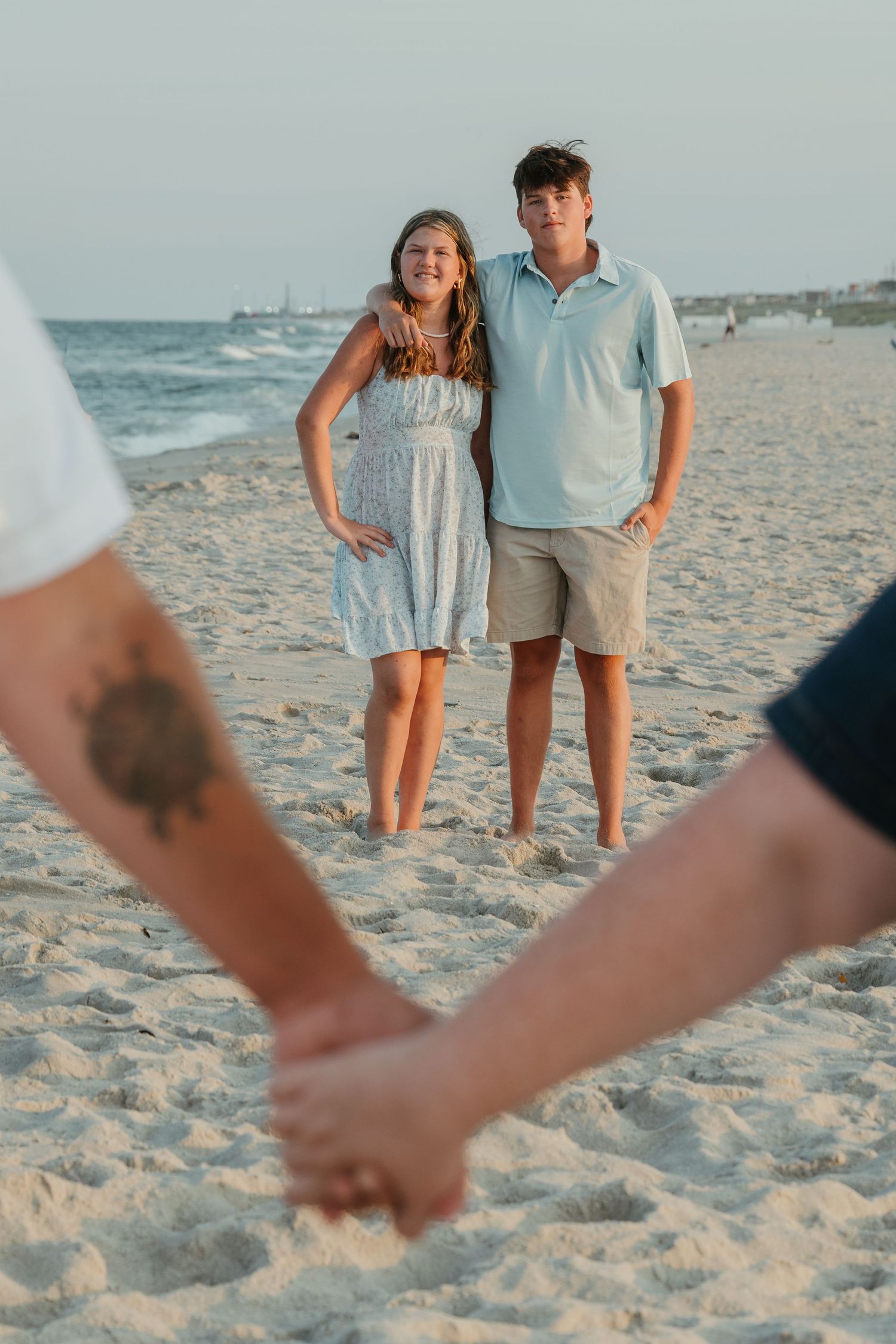 Couples pose for beach photos while holding hands on sandy shores at sunset.