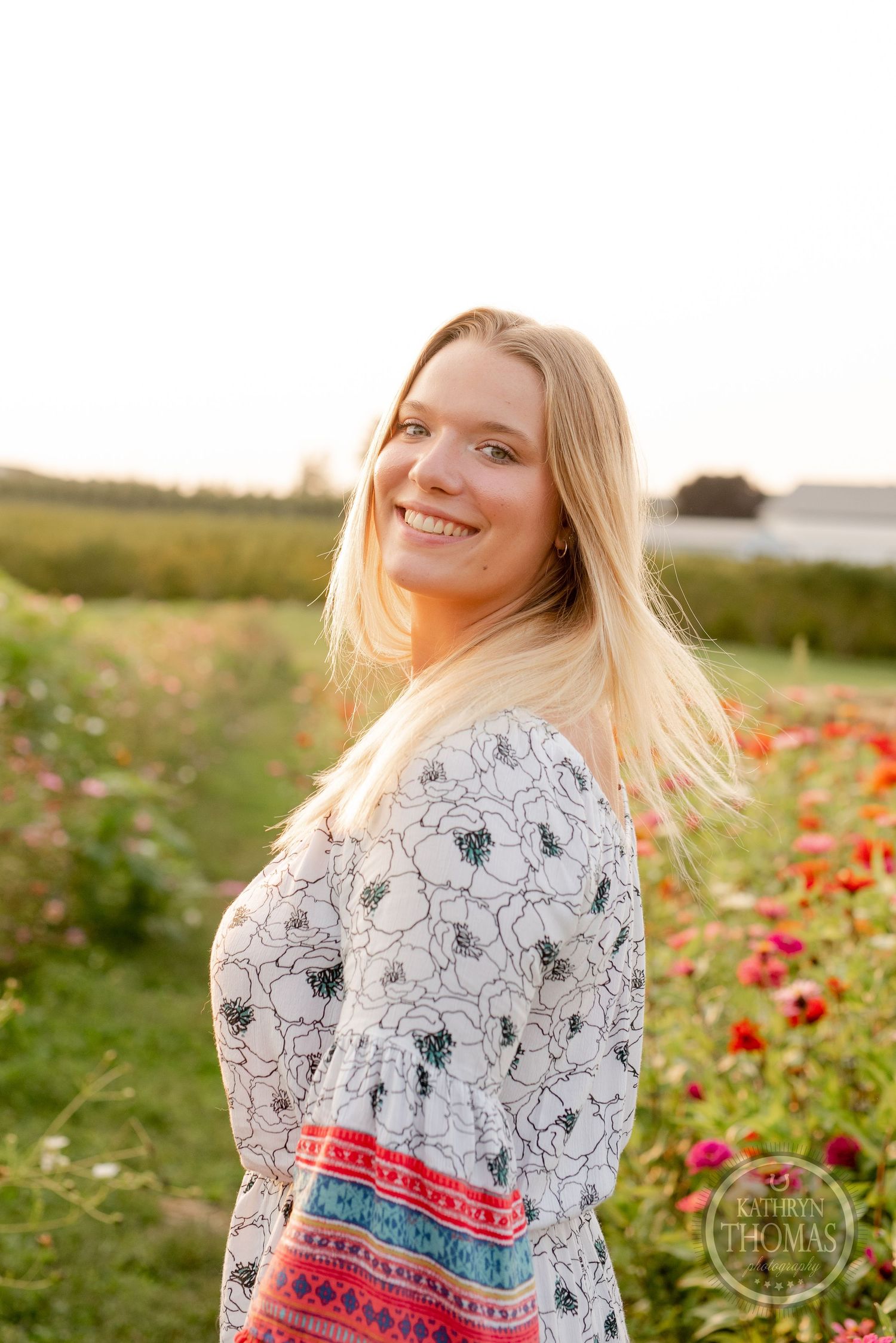 Natural sunset portrait in a floral print dress with flowing hair among wild poppies.