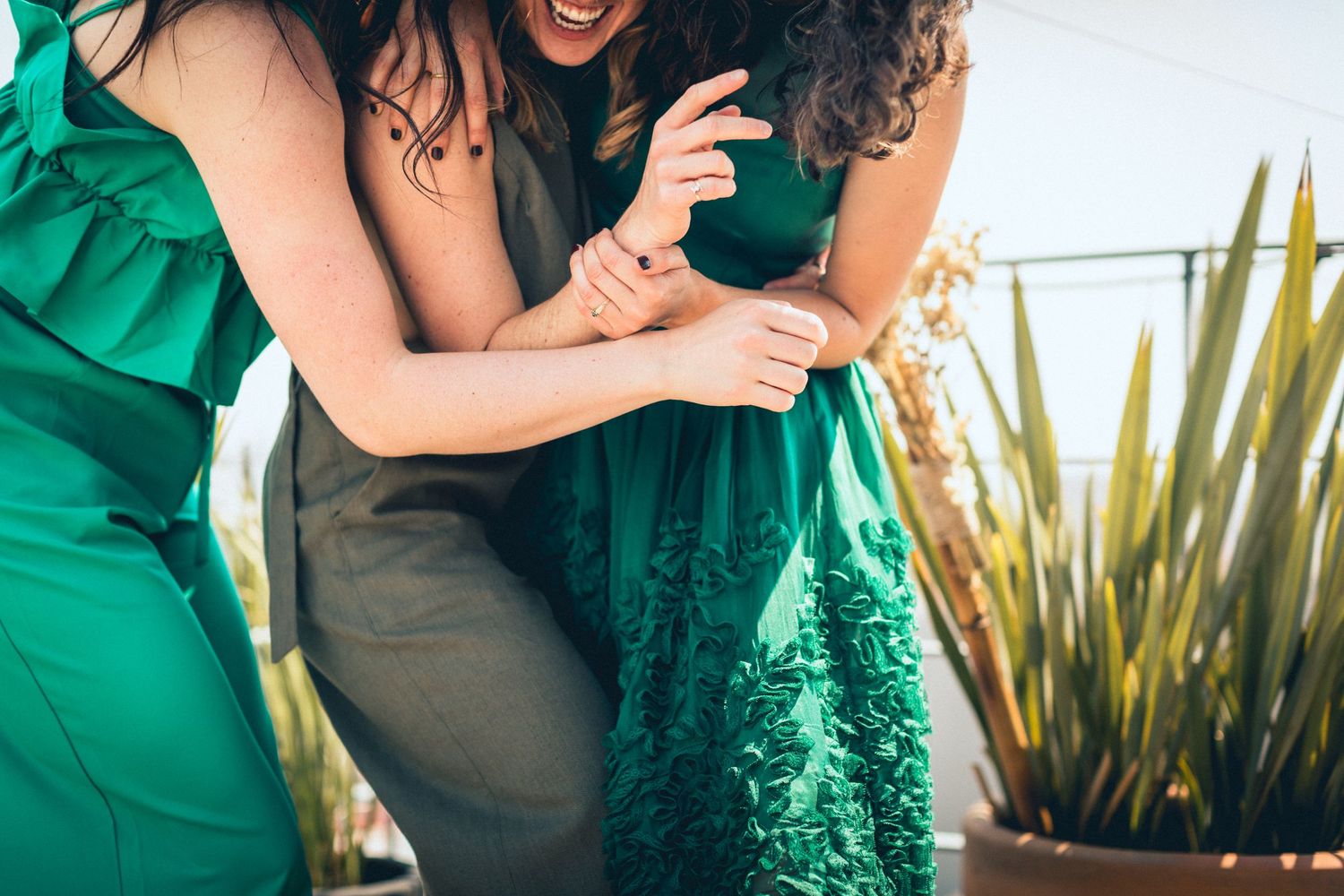 Wedding guests in green dresses laughing together at an outdoor celebration.