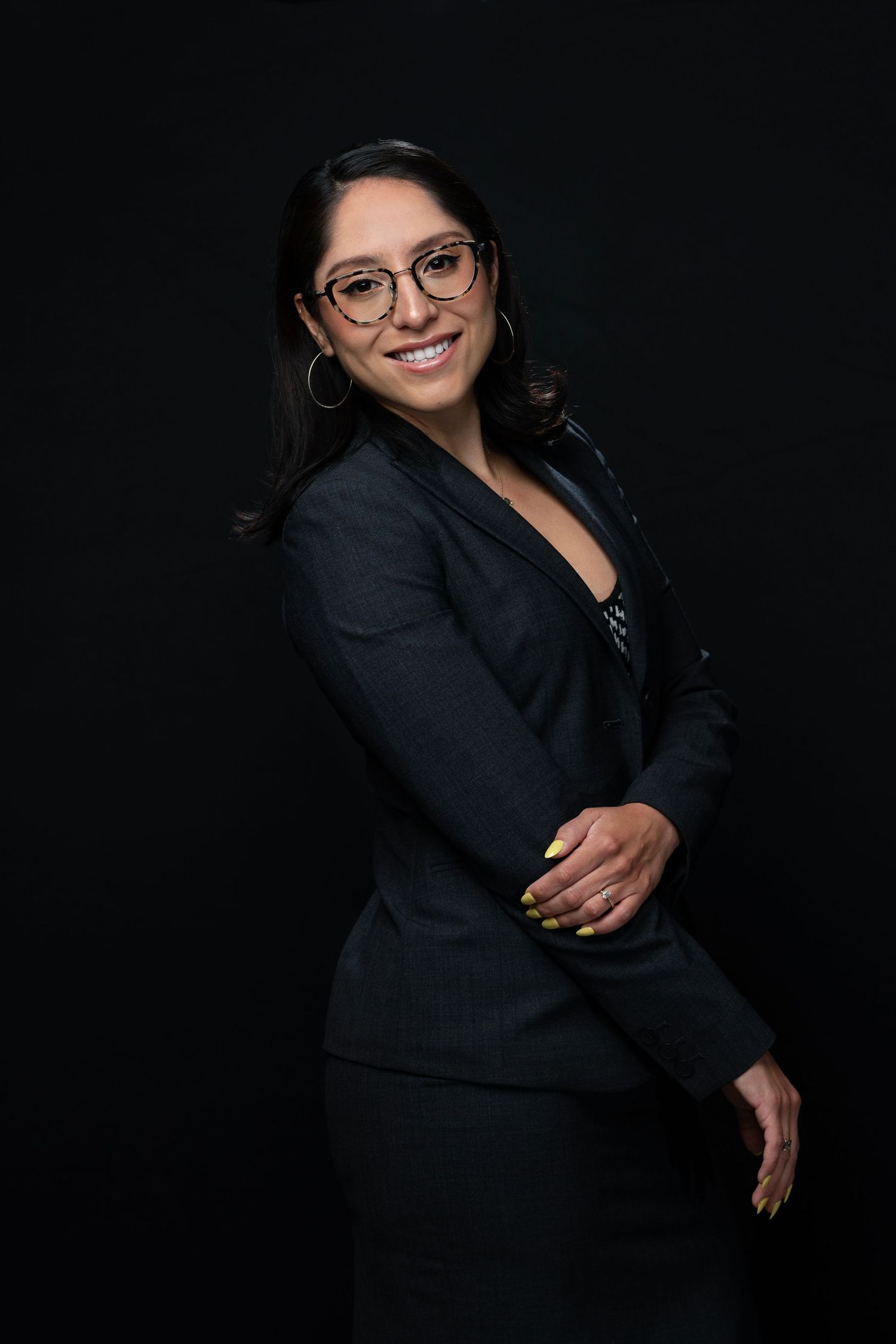 Professional portrait of woman in business suit and glasses against black background.