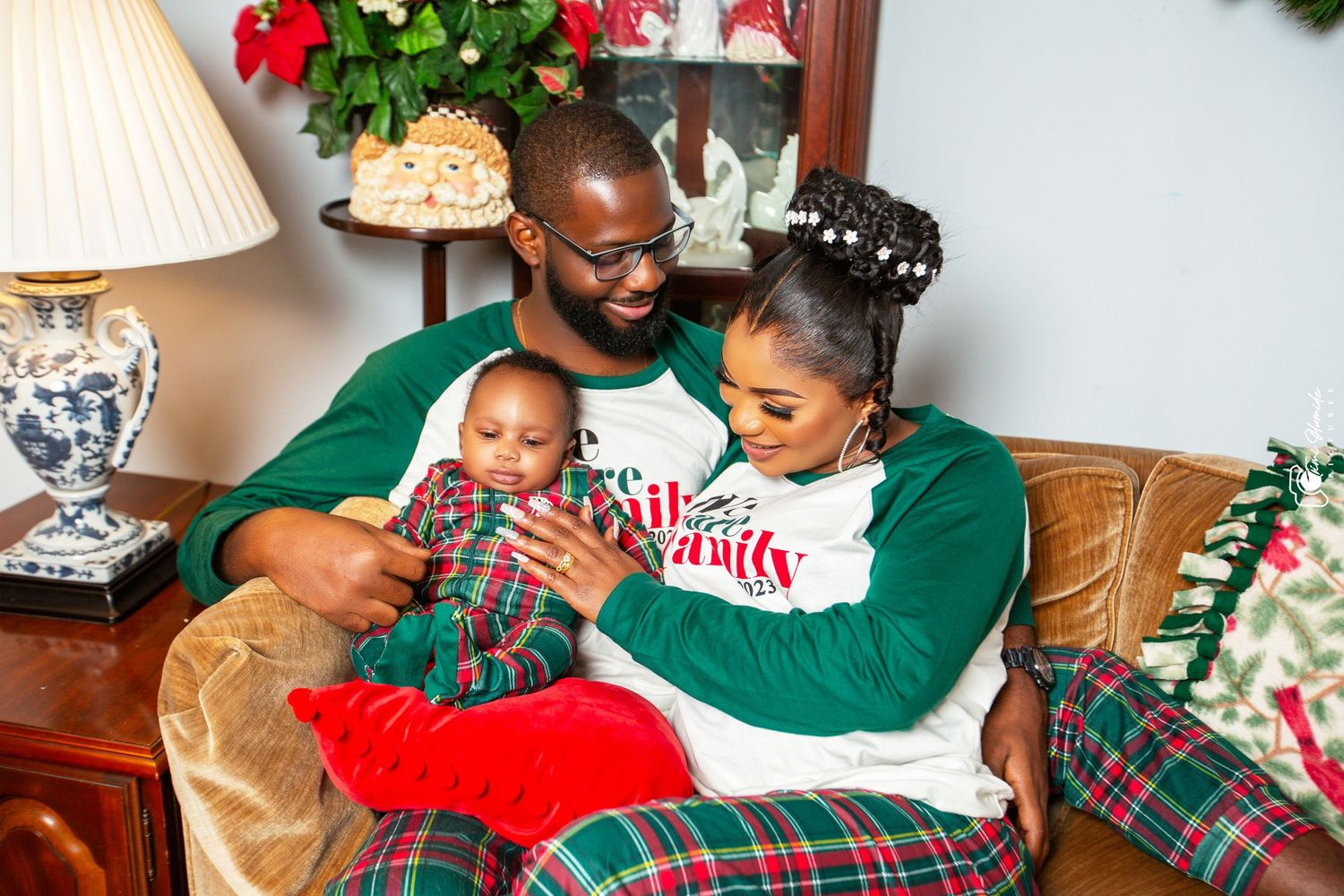 Family in matching Christmas outfits sitting together on tan couch with holiday decorations.