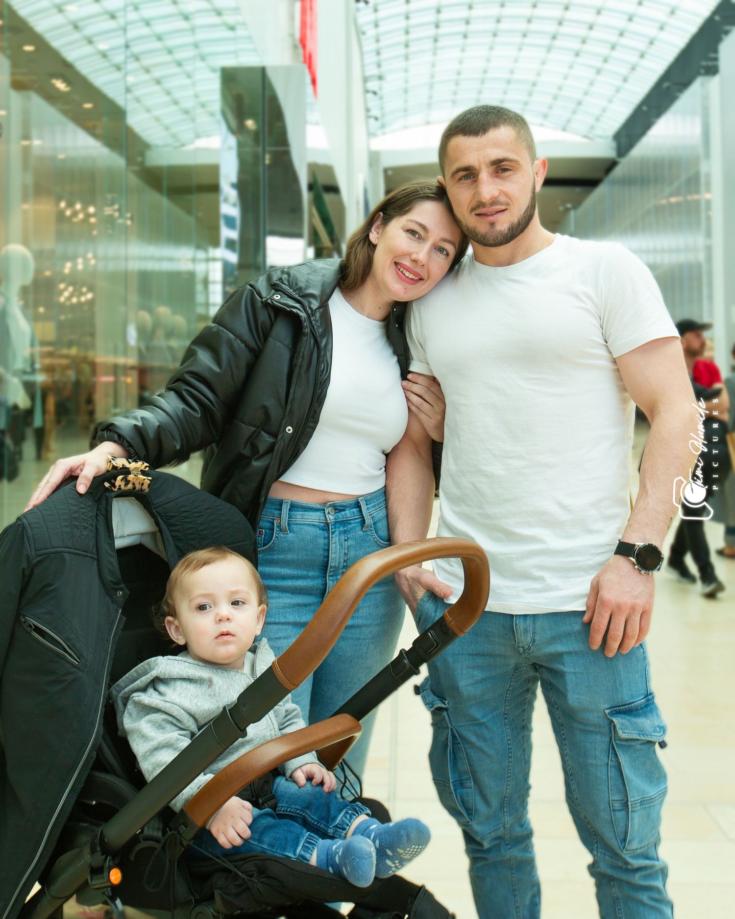 Family of three at shopping mall with young child in stroller.