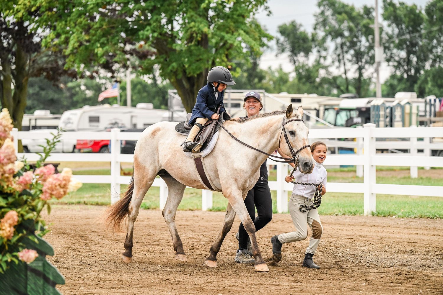 Buckskin pony trotting in a leadline class with little kid riding, kid leading the pony, and trainer alongside