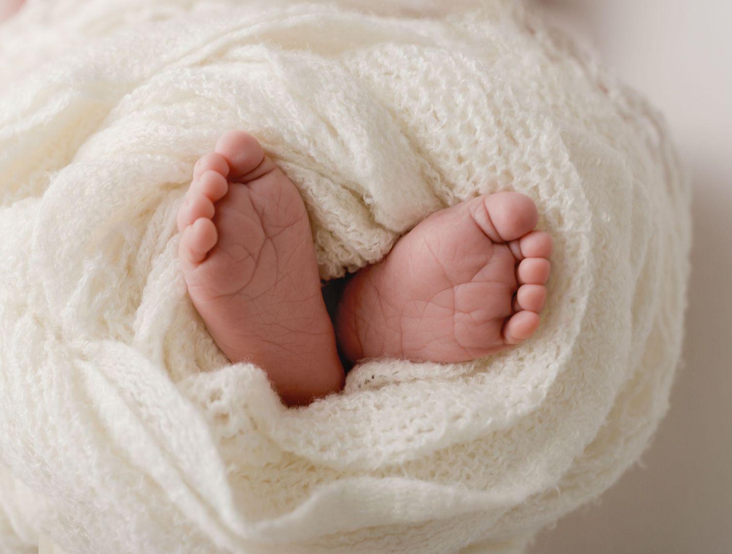 Tiny baby feet nestled in cream colored knit wrap.