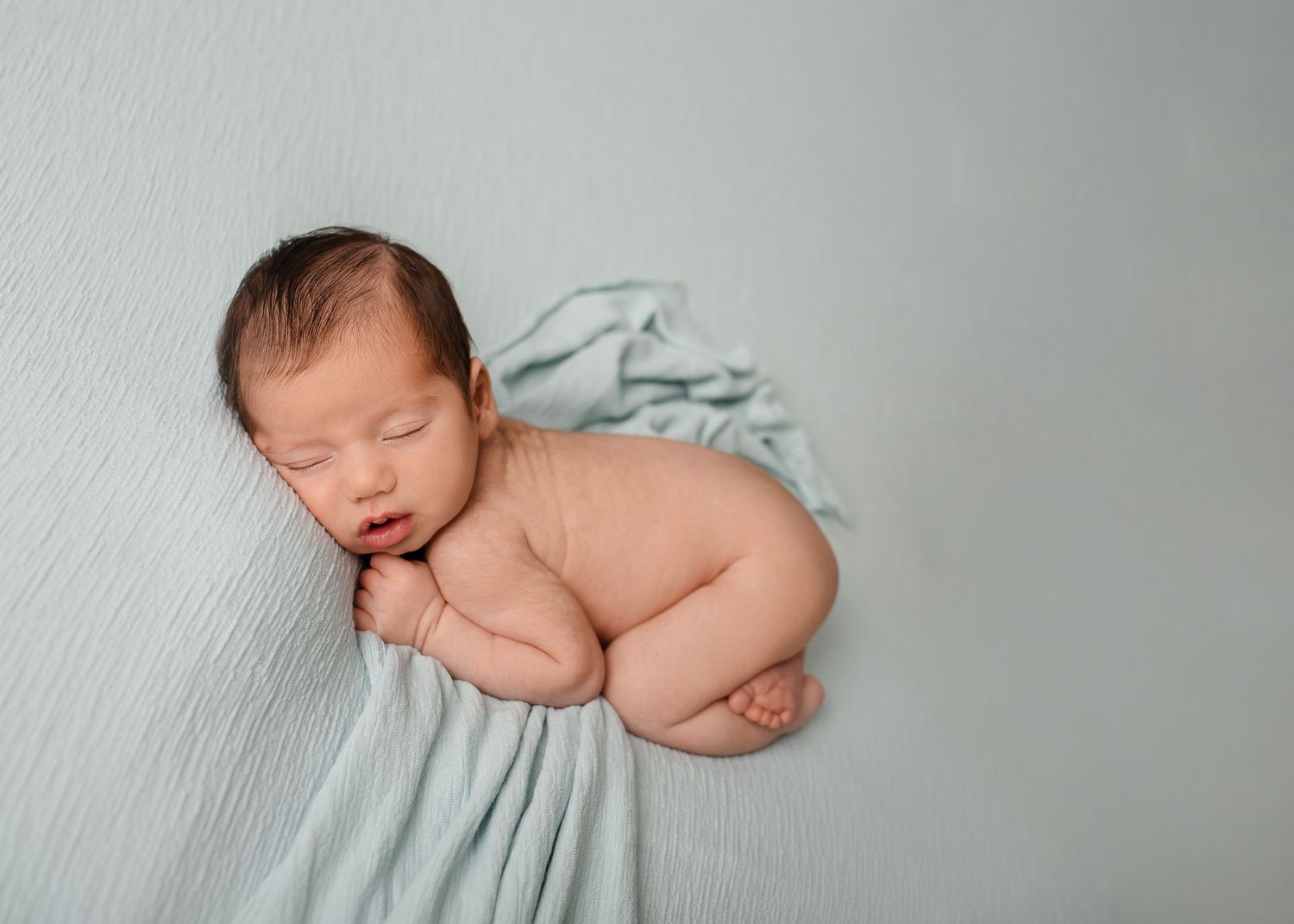 Sleeping newborn posed on soft mint fabric in minimalist style.