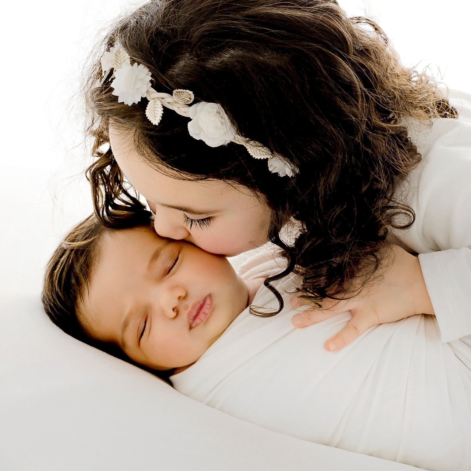 Peaceful sleeping child with floral hairpiece on white bedding.