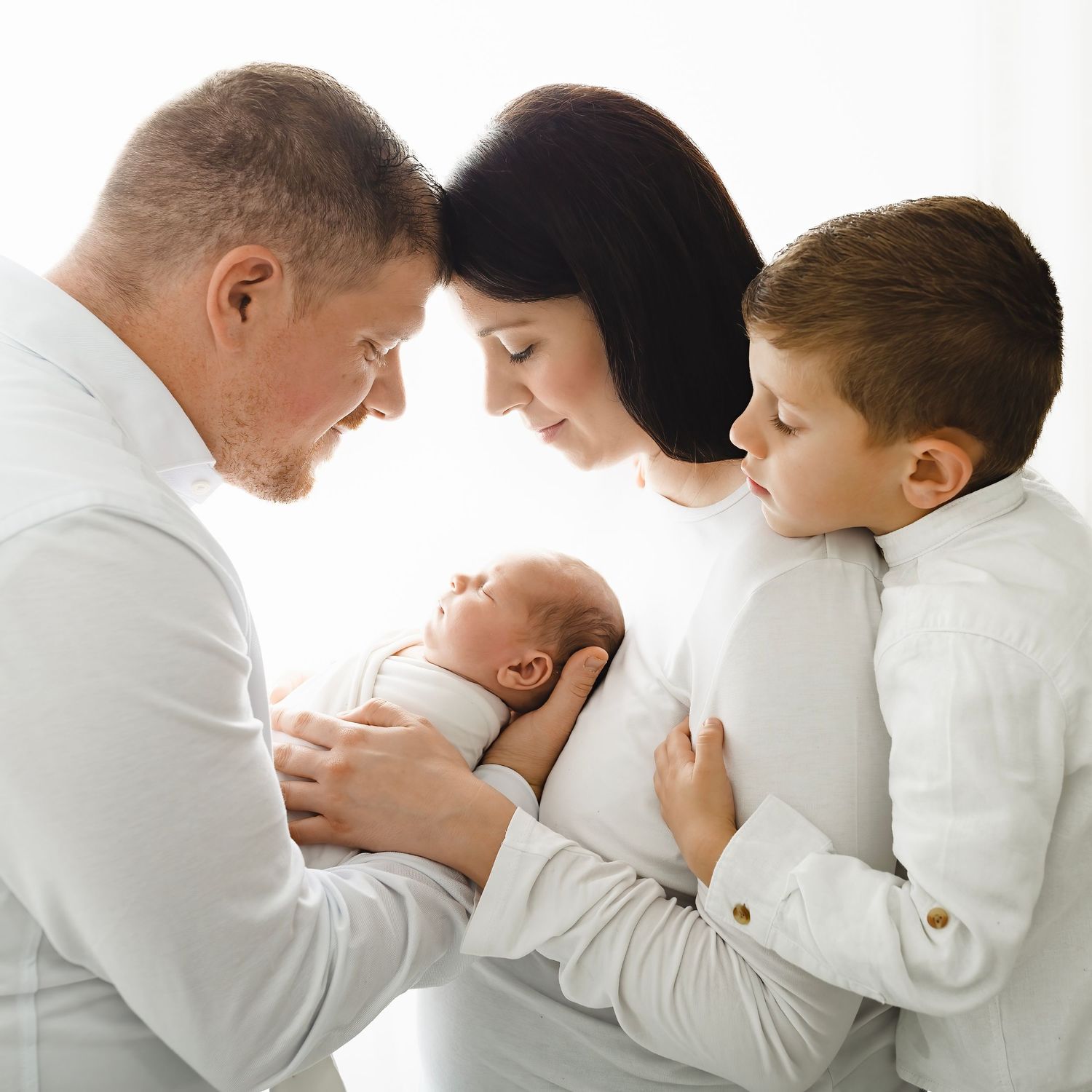 Family wearing white clothes embracing in intimate portrait series against white background.