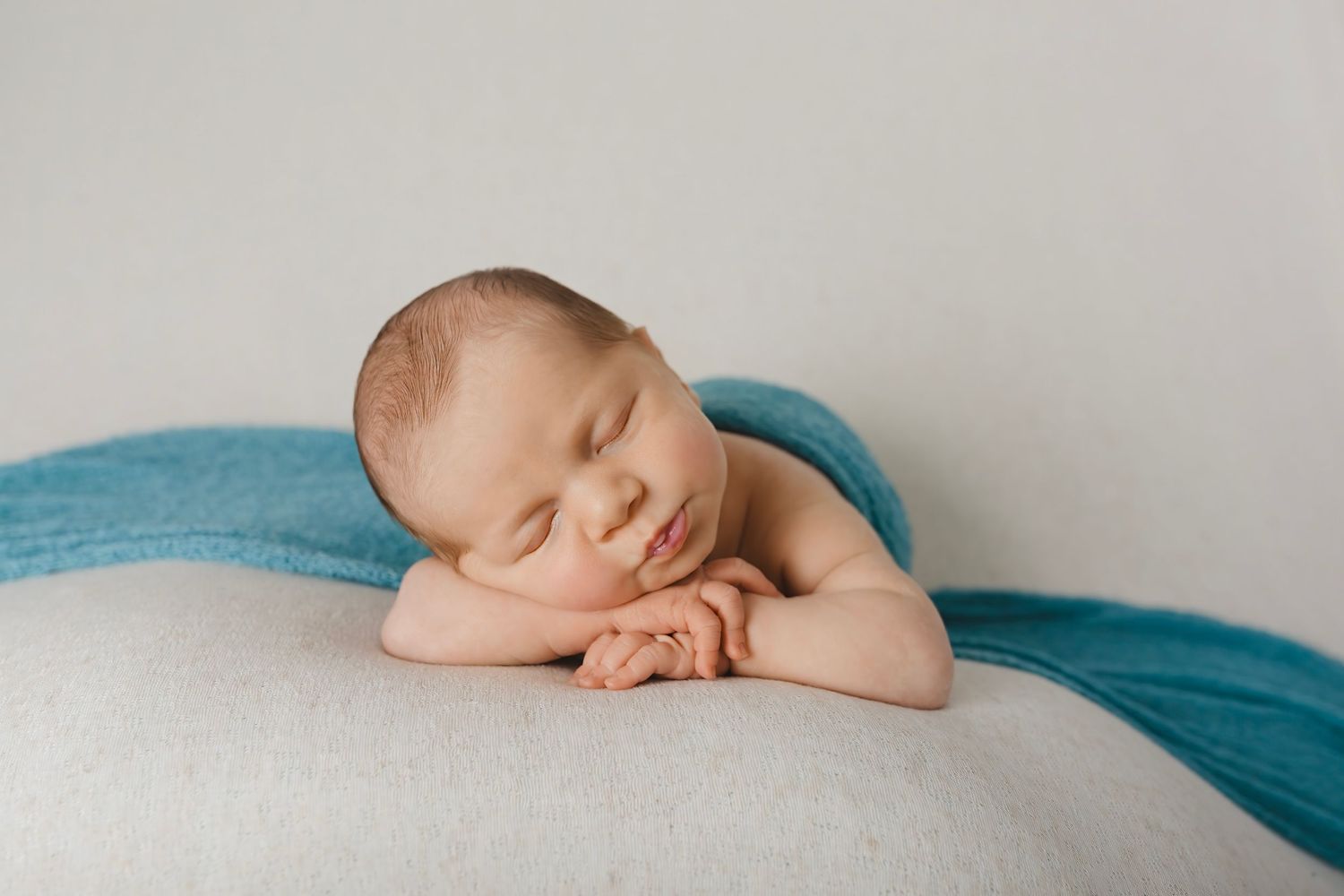 Sleeping newborn posed on blue fabric against white background in artistic composition.
