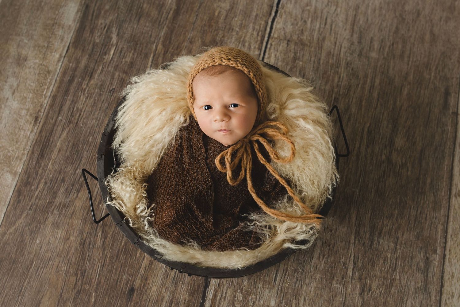 Newborn portraits on rustic wooden background with cream-colored fur accent.