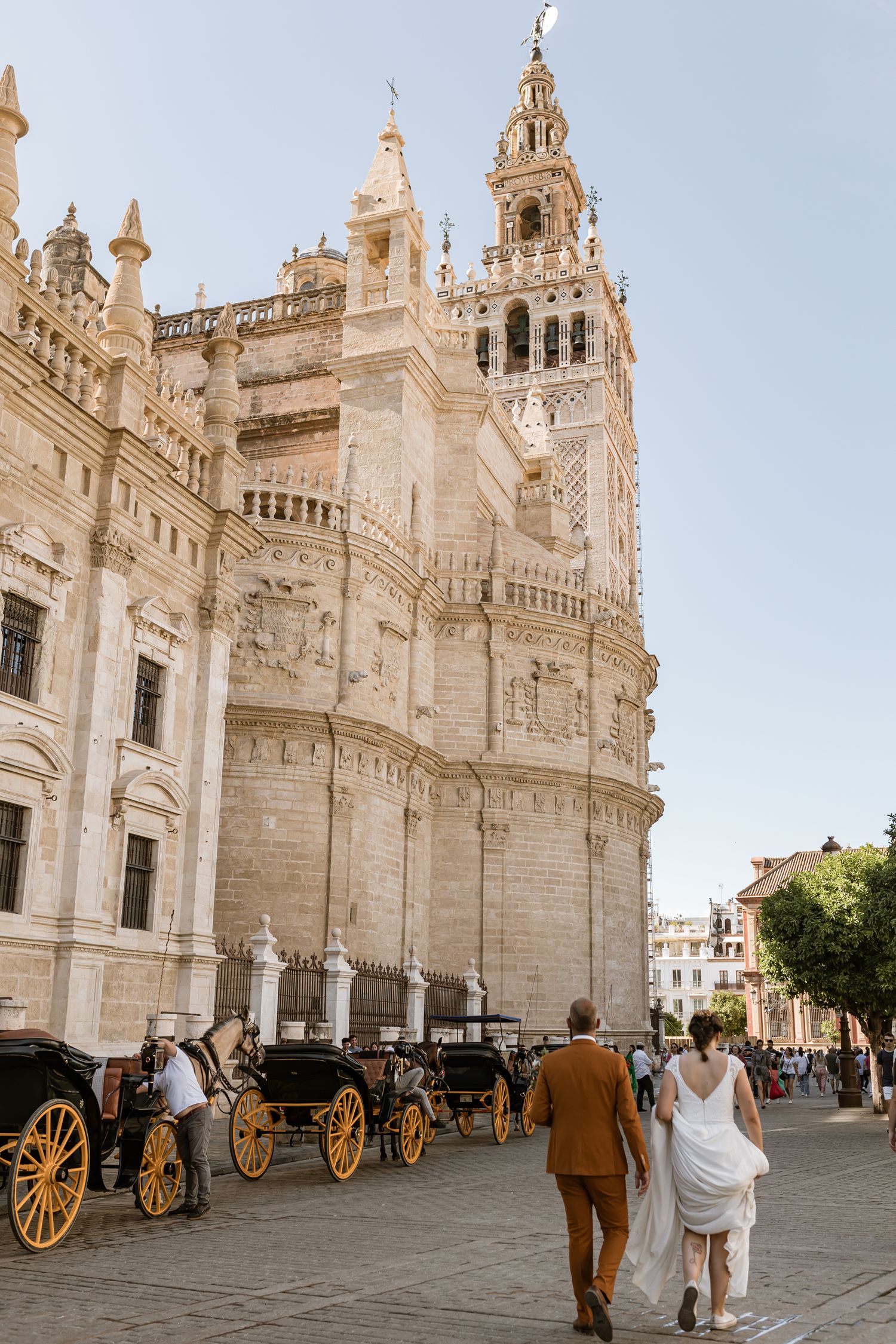 Ornate Seville Cathedral with horse-drawn carriages parked outside while people walk along its historic stone facade in Seville, Spain
