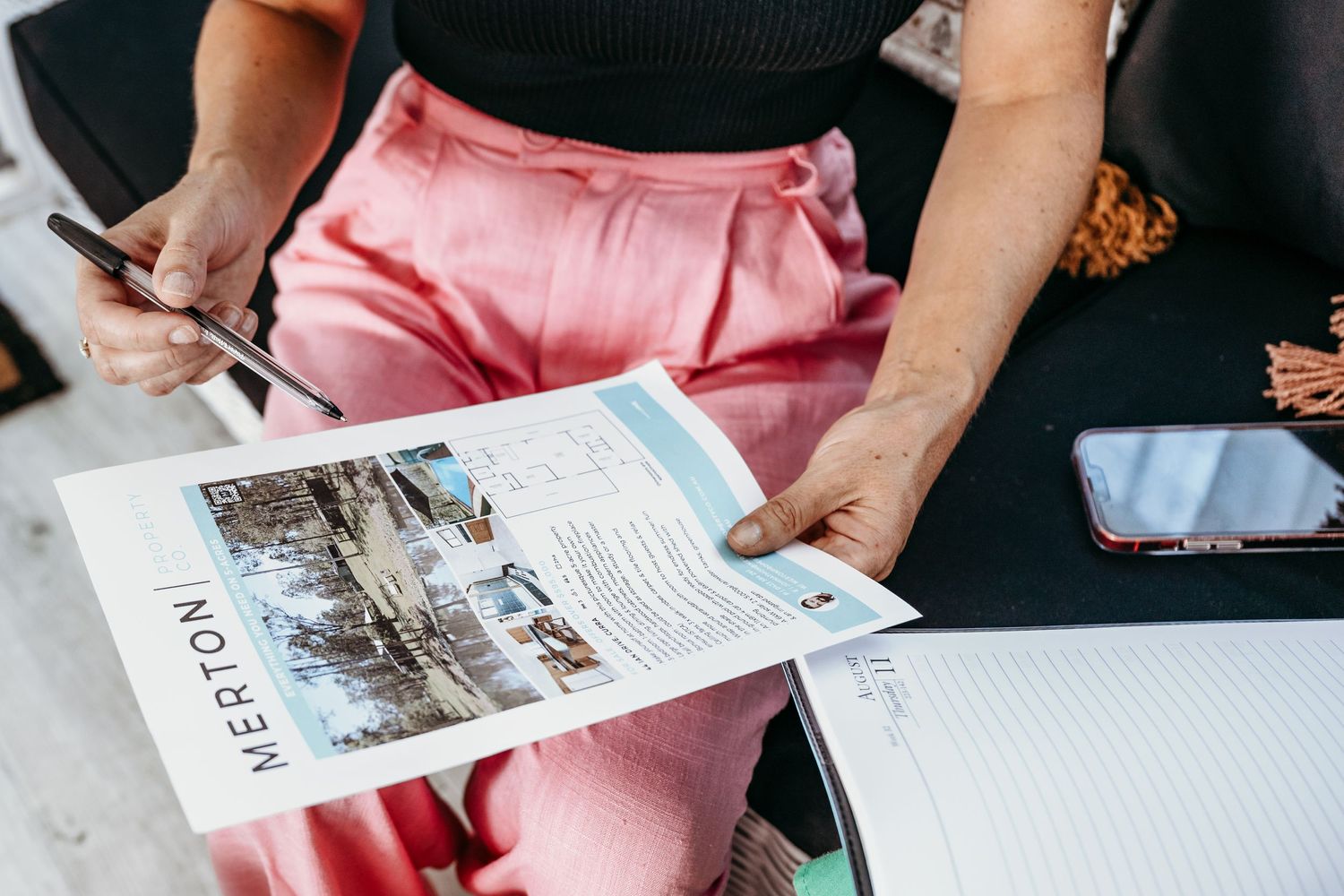 Person reading magazine with pink pants and taking notes.