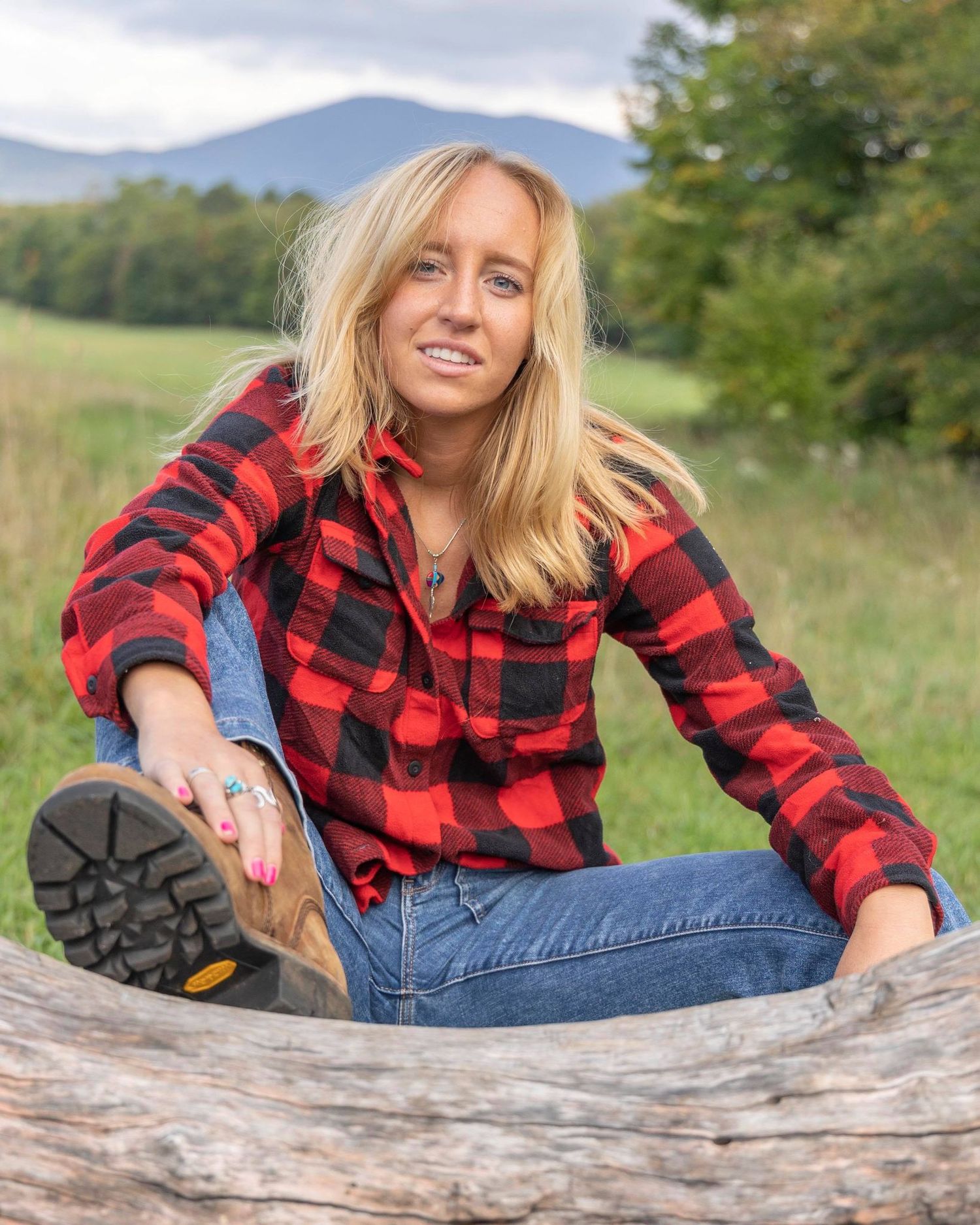 Figure in red buffalo plaid and jeans reclines on weathered log outdoors.