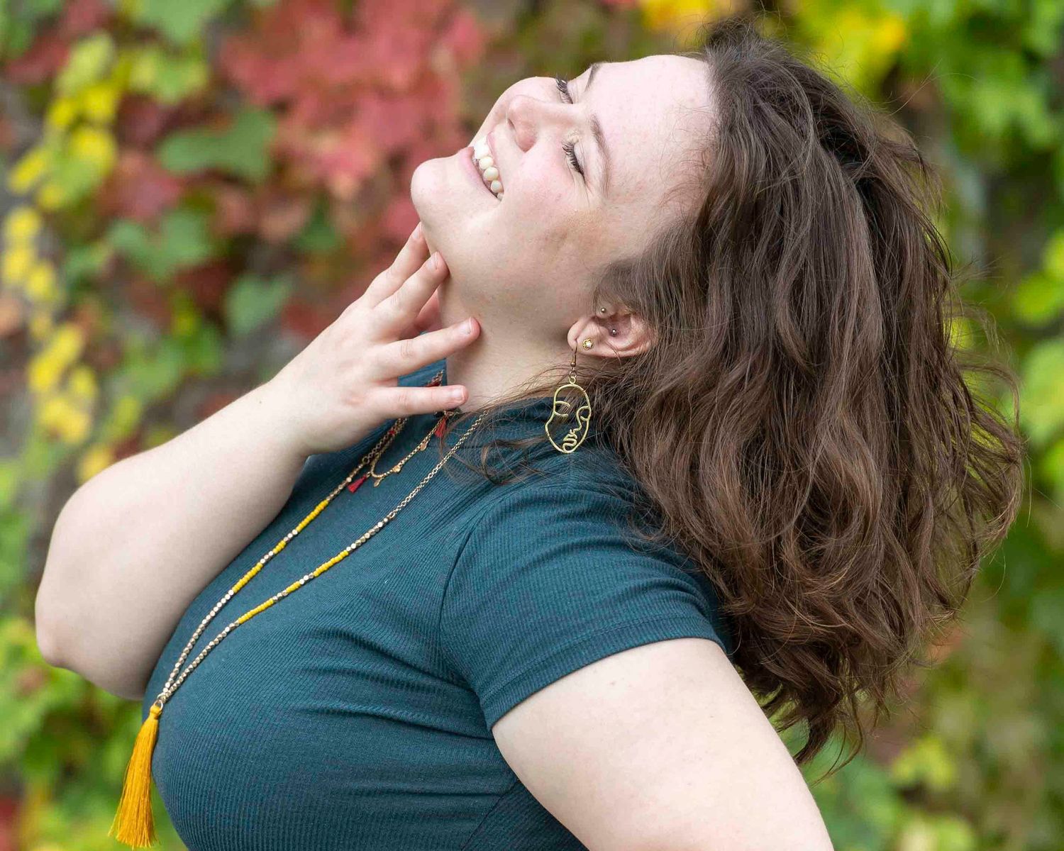 Joyful outdoor portrait in teal top with natural autumn foliage background.