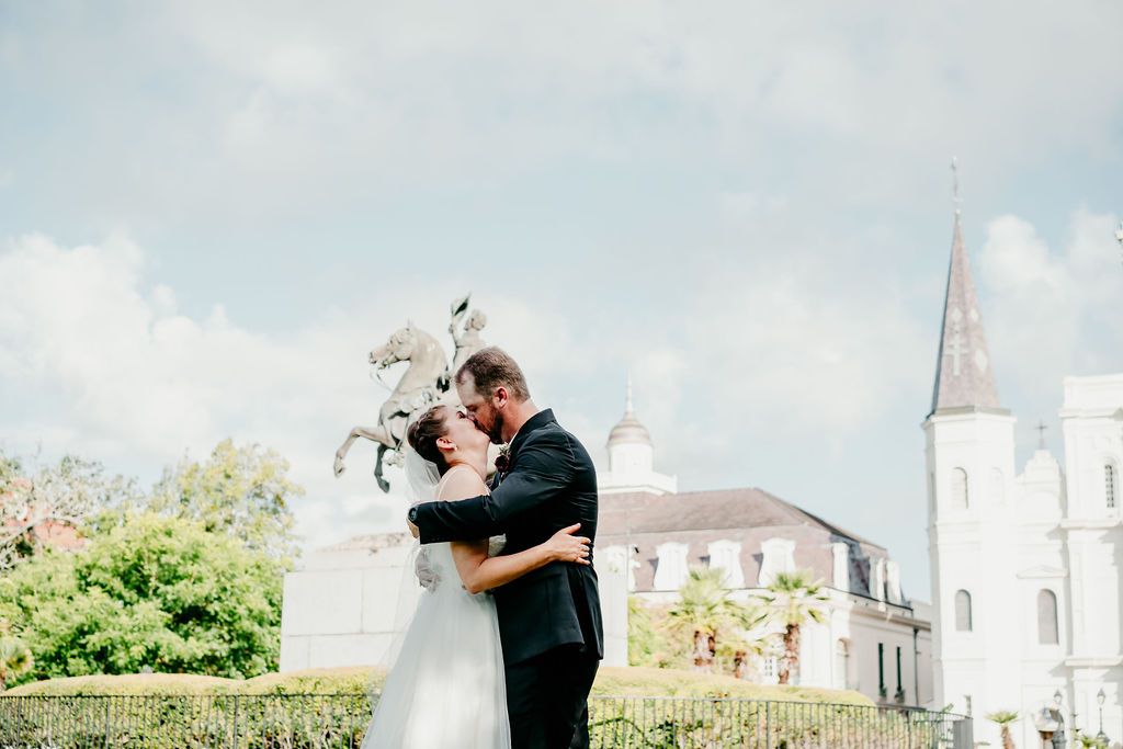 A couple kiss during their ceremony in Jackson Square with the cathedral behind them.