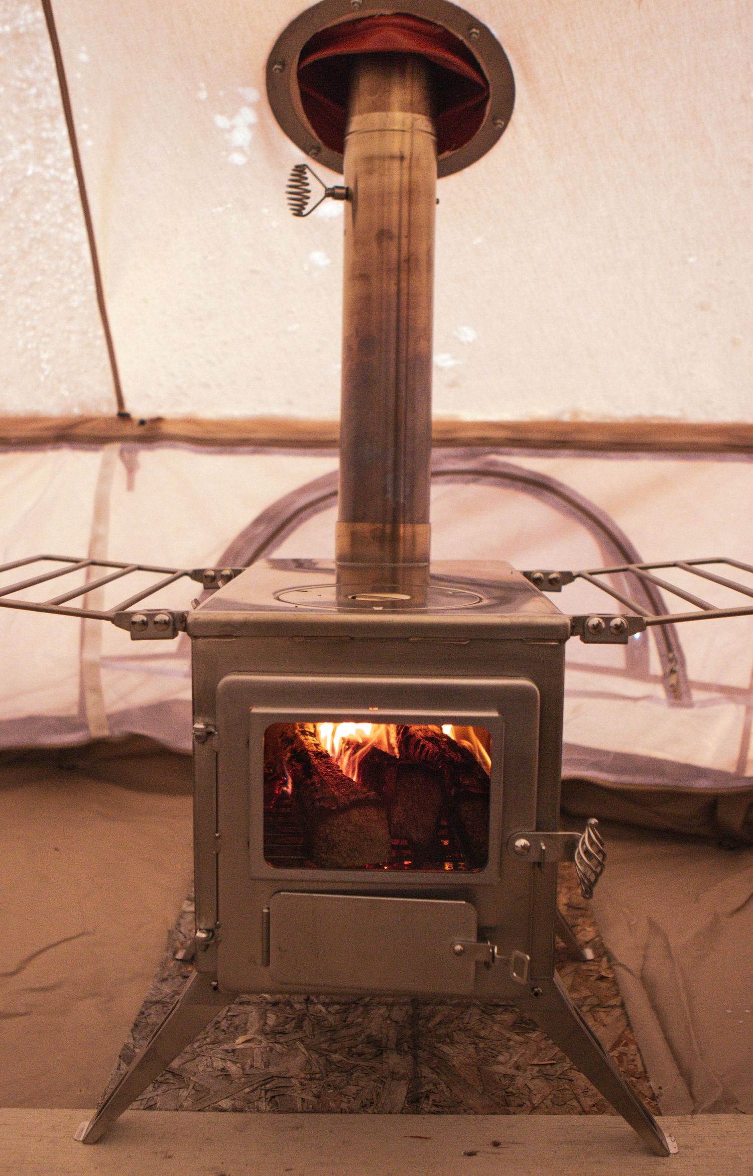 Wood burning stove with tall chimney pipe installed inside canvas tent.