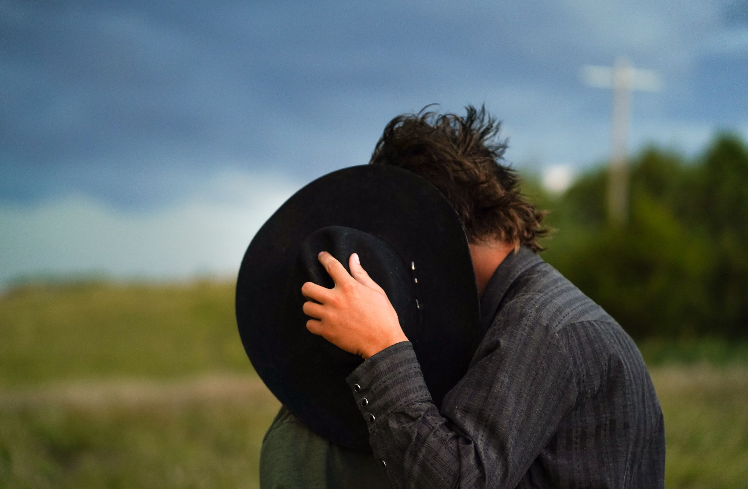 A couple shares an intimate moment while sitting in tall grass against a blue sky.