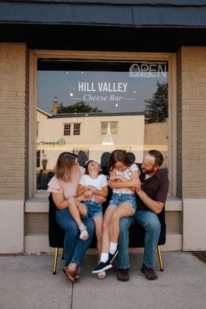 Family relaxing together outside Hill Valley Cheese Bar storefront.