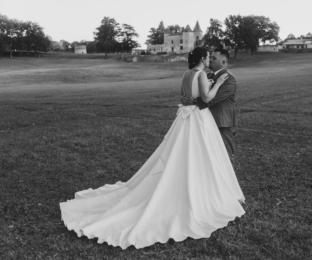 Black and white wedding photo of couple embracing on grass with building in background. photographe mariage Bordeaux gironde