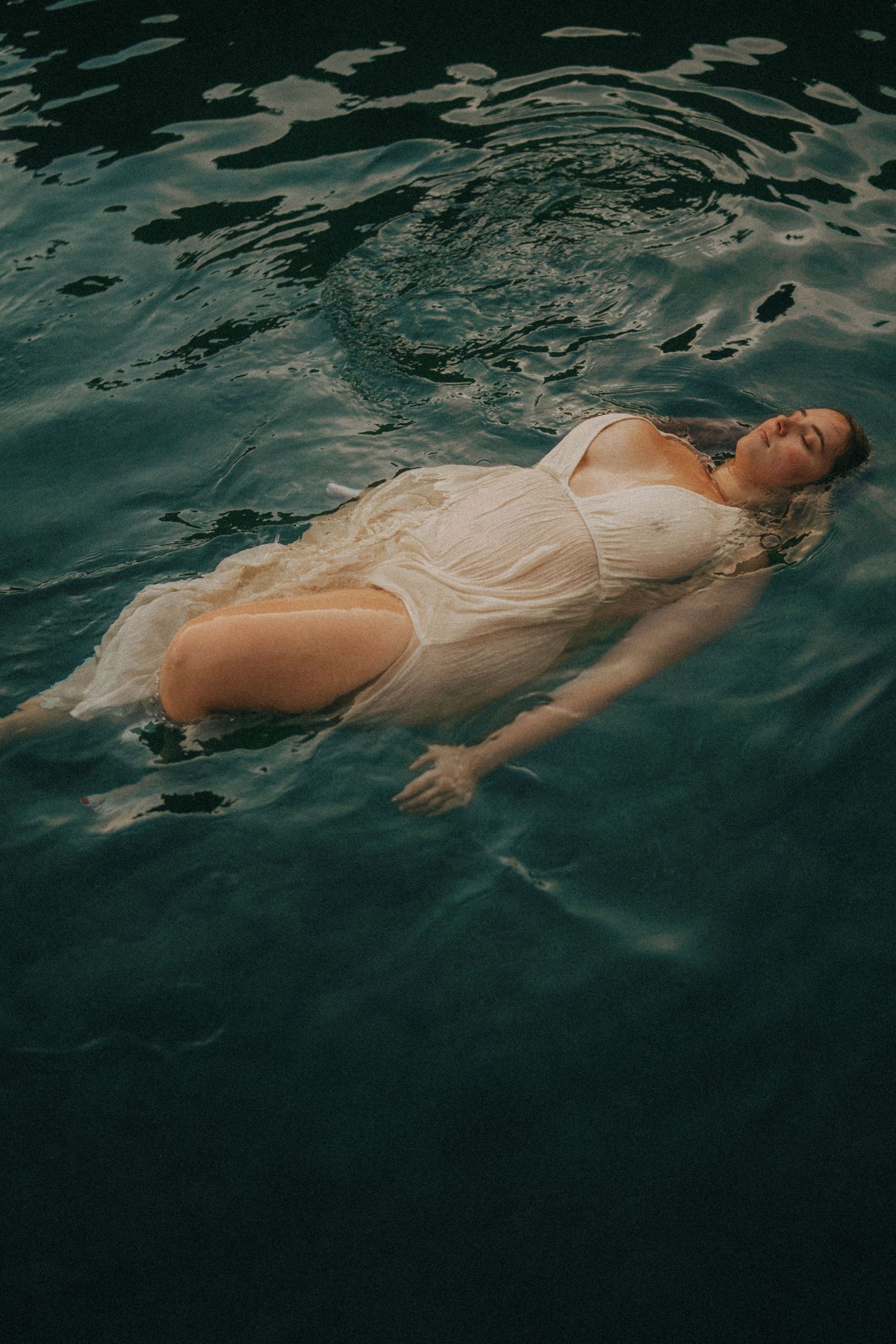 Figure floating in dark blue water wearing light colored clothing.