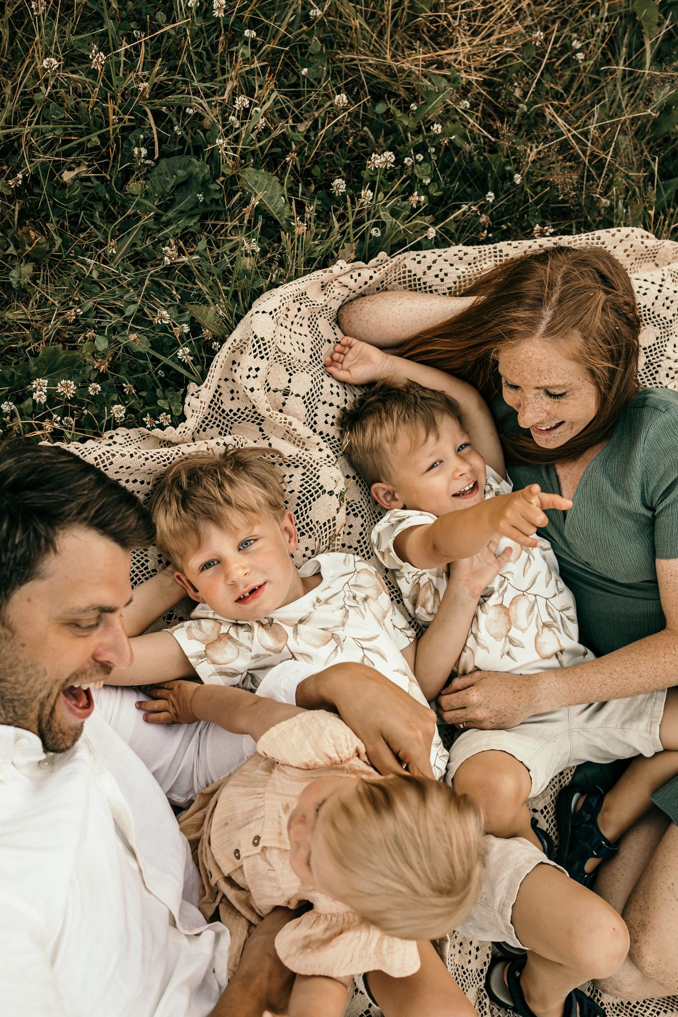 Mysig familjefotografering på sommaren där familjen ligger på en filt tillsammans.