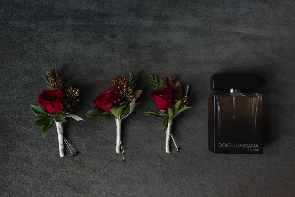 Three red rose boutonnieres and cologne bottle arranged on dark background.