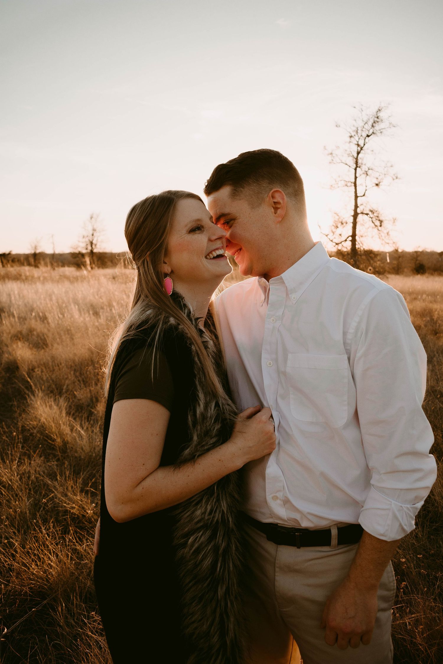 Intimate moment between a couple sharing laughter in a golden field at dusk.