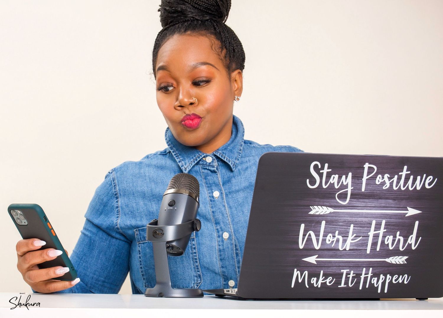 Content creator setup with microphone, laptop and motivational sign in denim shirt.
