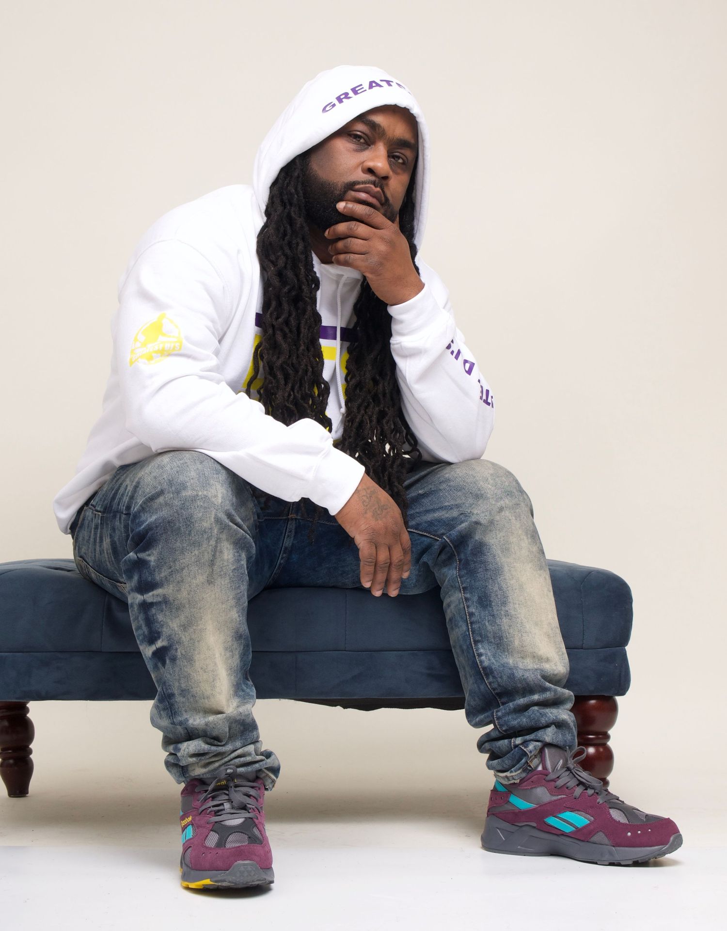 Casual portrait in white hoodie and distressed jeans sitting on blue couch.