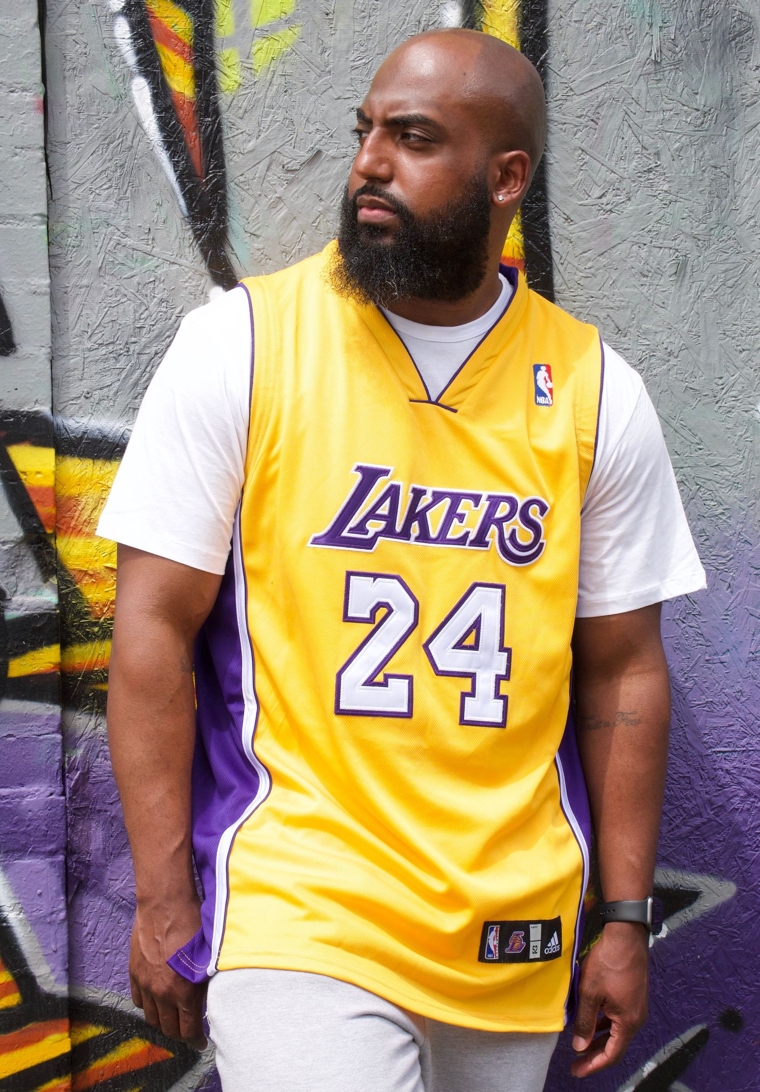 Basketball fan wearing yellow Lakers jersey number 24 poses against graffiti wall.
