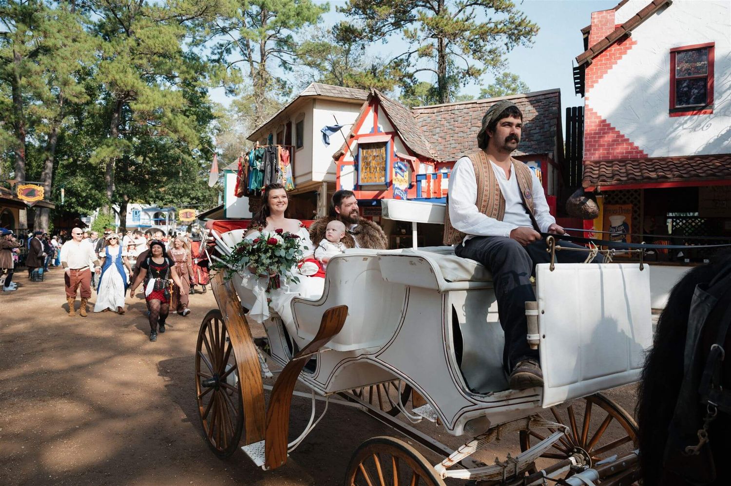 White horse-drawn carriage transports visitors through a Renaissance festival grounds.