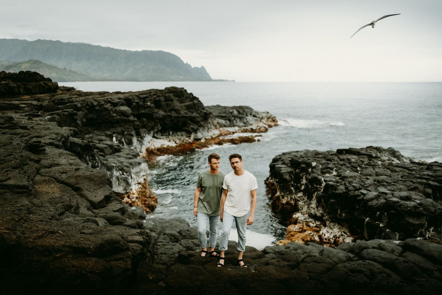 Couple exploring rocky coastal cliffs with seabird soaring overhead.