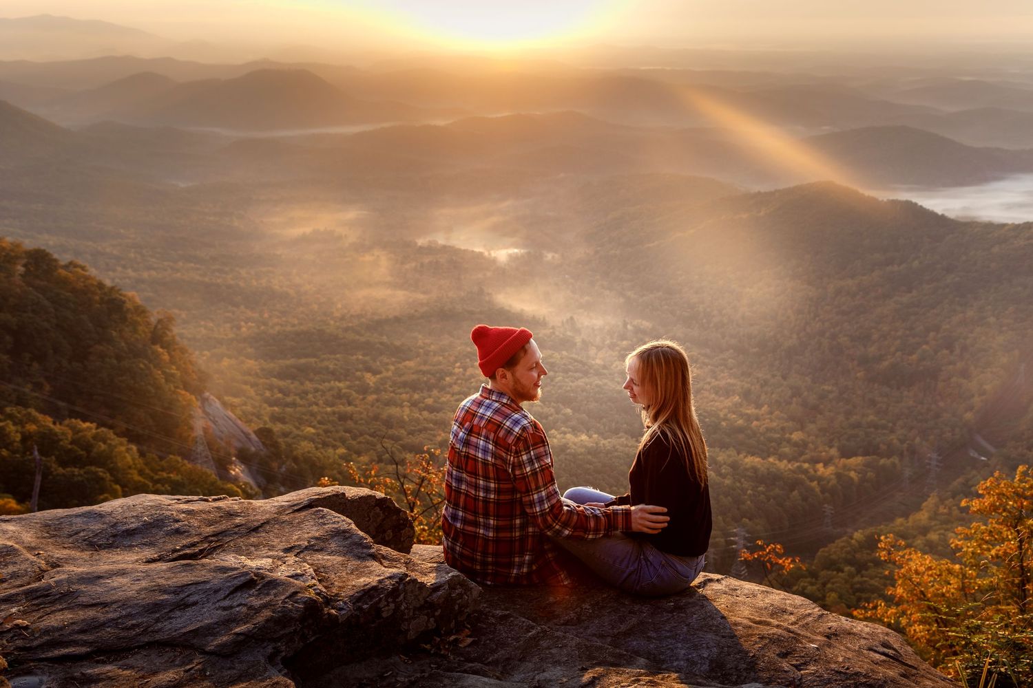 Two people share a romantic moment while watching sunset from a mountain overlook on a misty autumn evening.