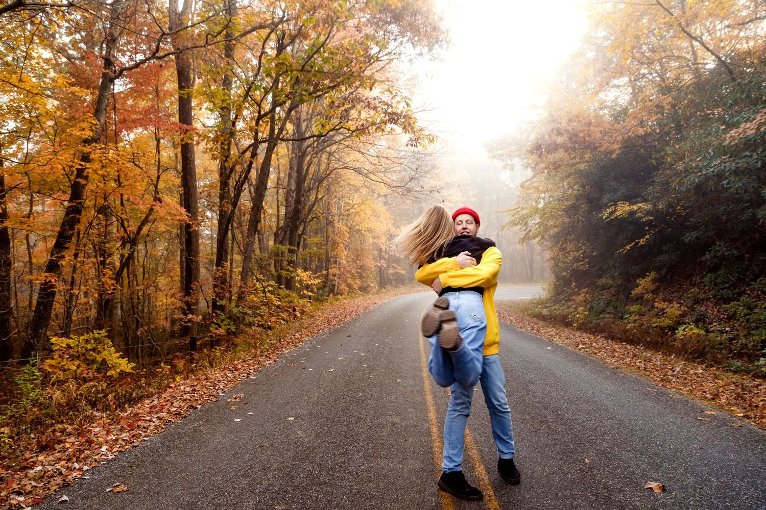 Joyful moment captured on tree-lined autumn road with golden sunlight filtering through.