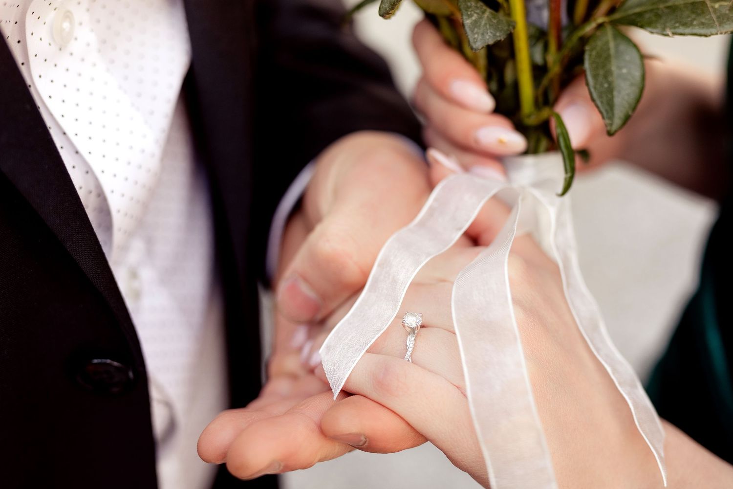 Close-up detail of hands during wedding ceremony with white lace and floral elements.
