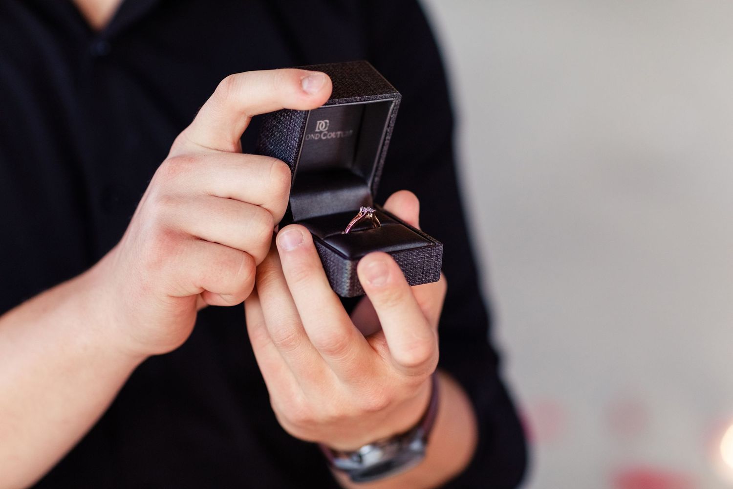 Hands holding an open ring box against a dark background.