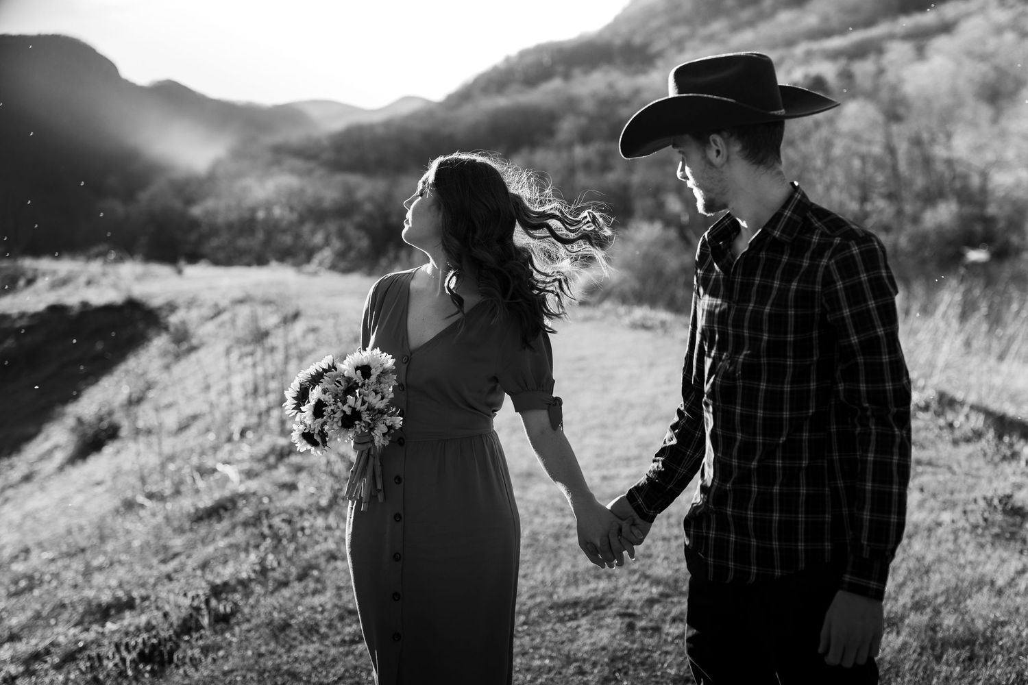 A romantic black and white portrait of a couple on a mountain trail at sunset.