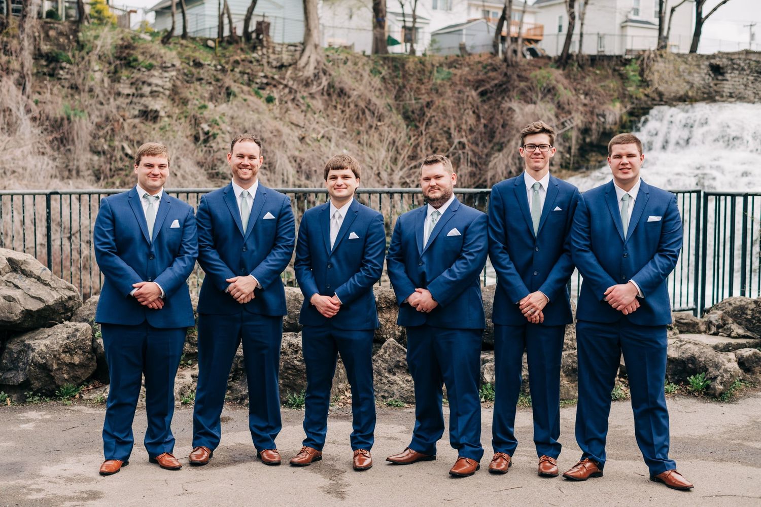 groom and groomsmen in navy suits posing for portraits in front of a waterfall