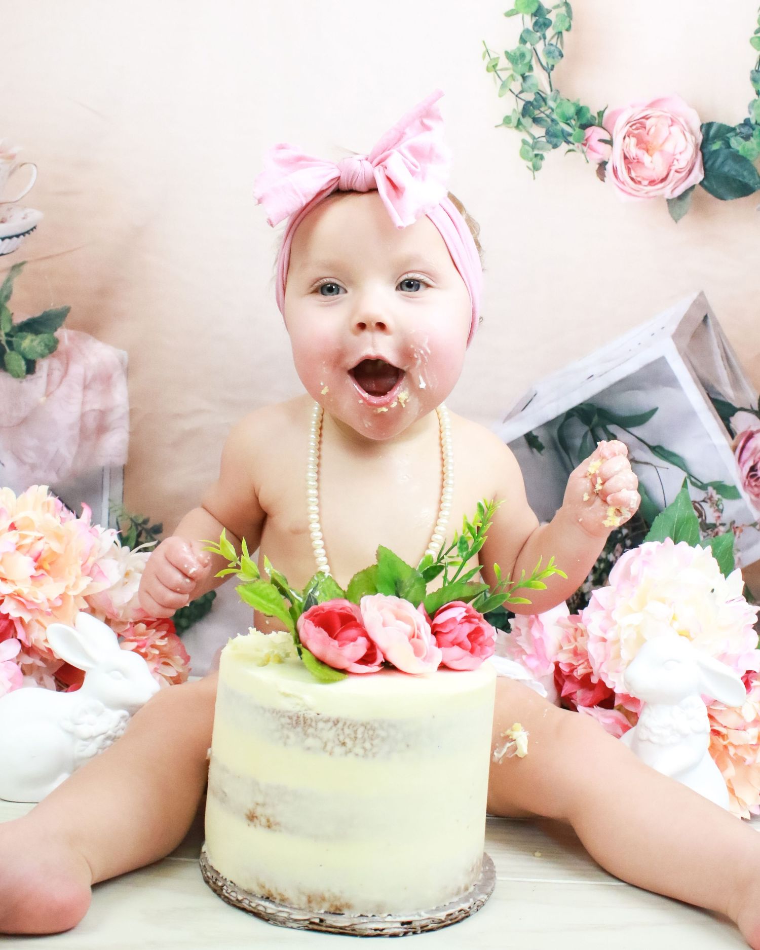 Cake smash photo session with pastel green cake and pink floral decorations.