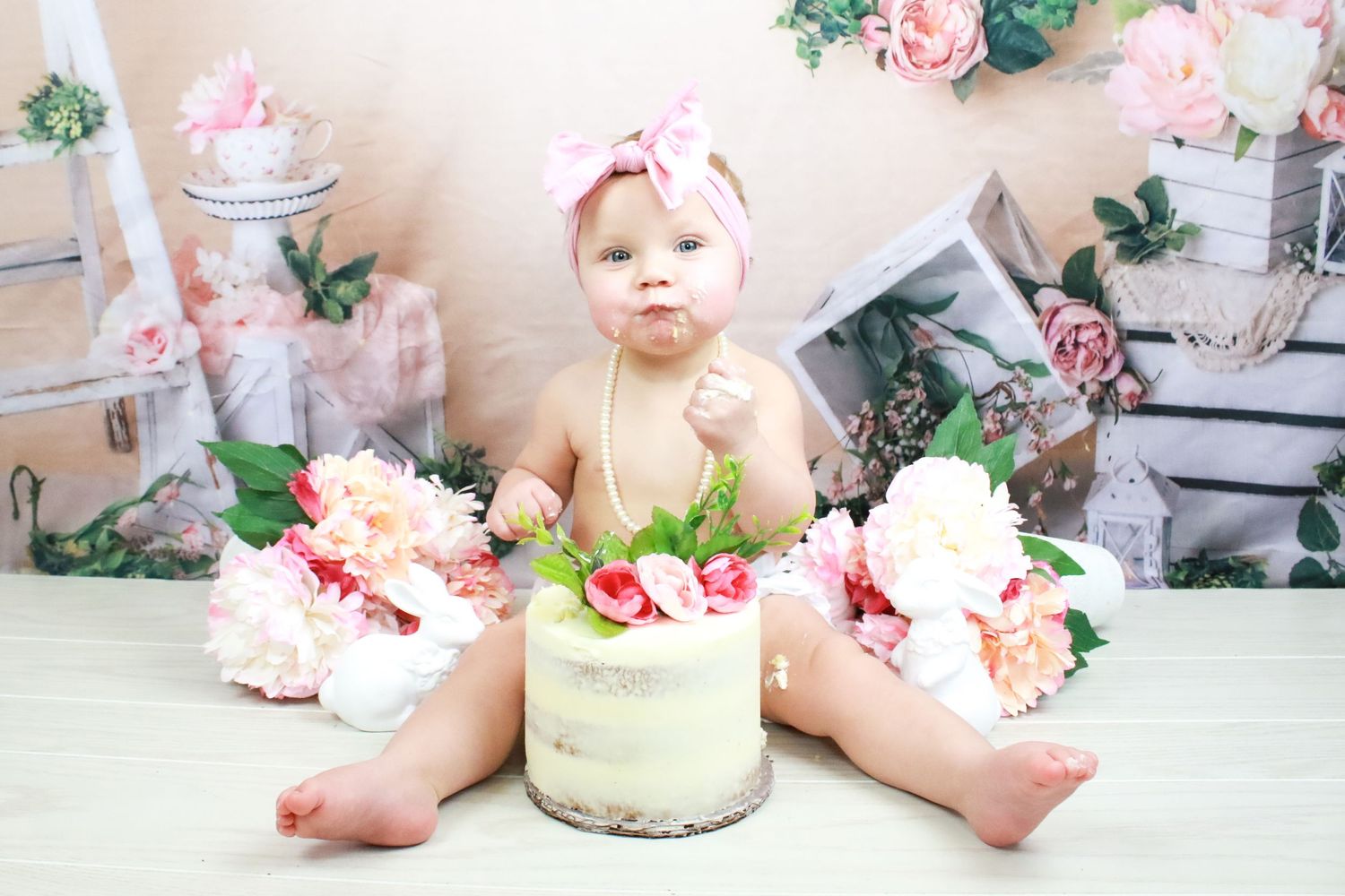 Cake smash photography session with floral backdrop and vintage decorations.