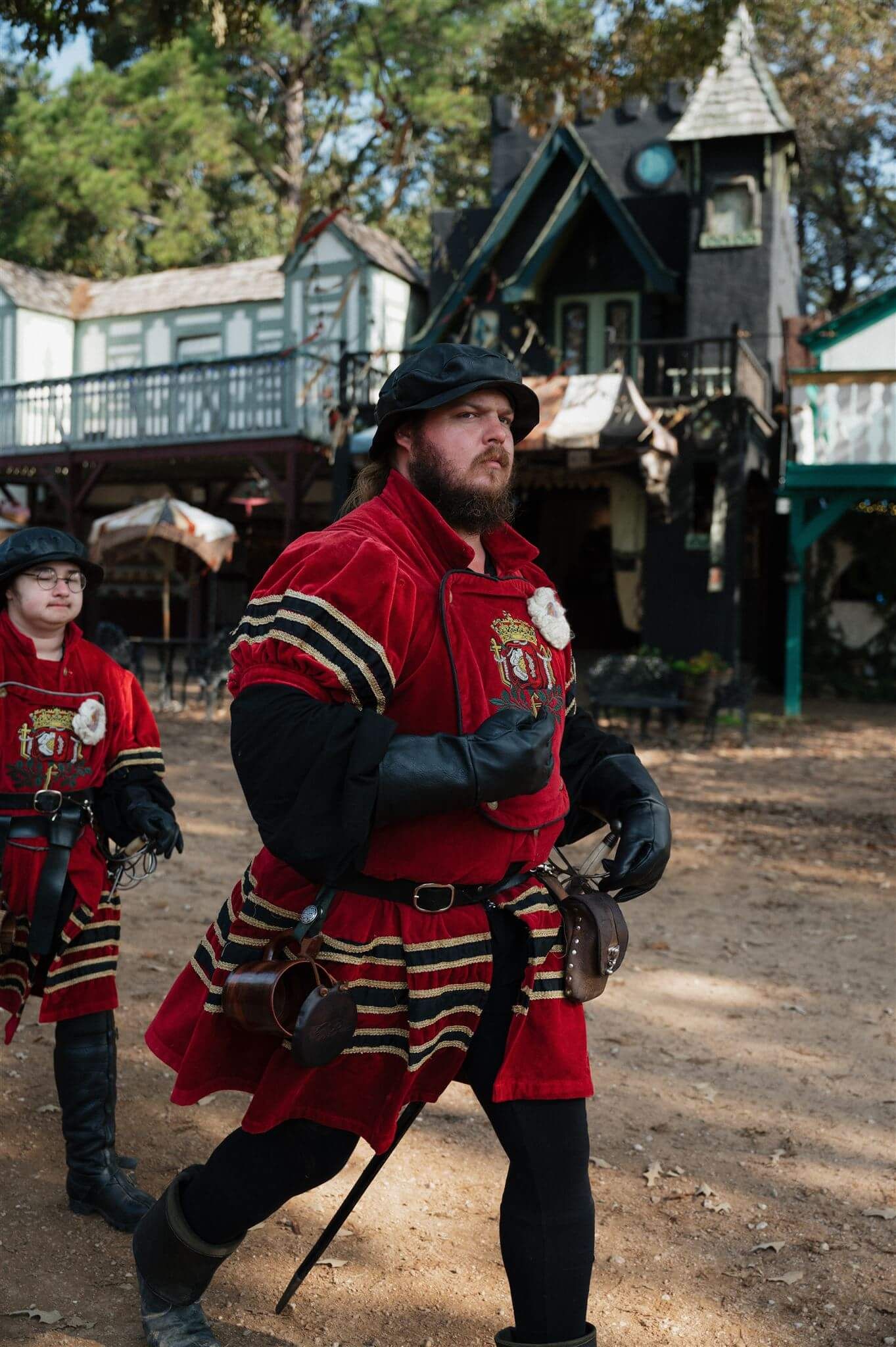 Guard in red and black Renaissance costume stands watch at medieval festival.