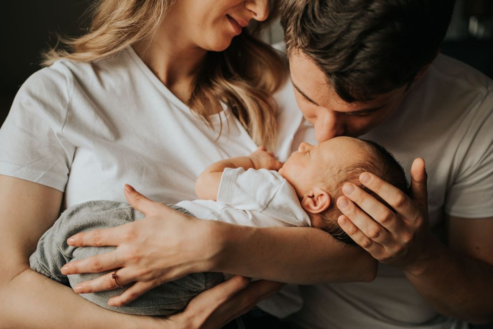 mama trzyma dziecko, tata obejmuje główkę i całuje - sesja rodzinna Kraków