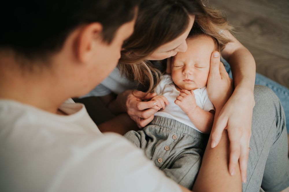 noworodek leży na kolanach taty, mama i tata go obejmują - sesja noworodkowa Kraków